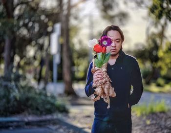 Portrait of young asian man holding bouquet of tulips against plants and trees