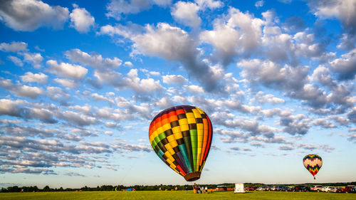 Colorful hot air balloons over field against cloudy sky