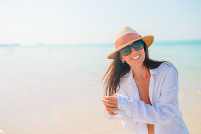 Woman wearing sunglasses standing at beach against sky