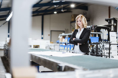 Blond businesswoman standing on shop floor, looking at plans