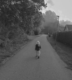 Rear view of woman walking on road amidst trees