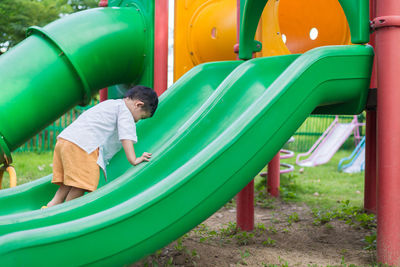 Rear view of boy playing on slide at playground