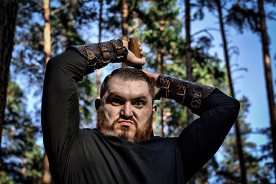 Portrait of angry man holding axe against trees in forest
