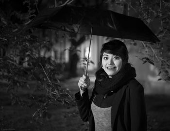 Portrait of smiling young woman holding umbrella at night