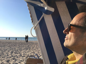 Close-up of man wearing sunglasses hooded chair at beach against sky