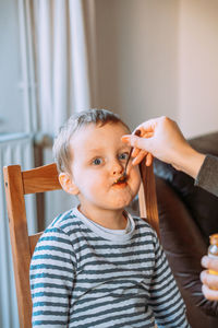 Mom feeds a little boy with a spoon. the boy is sitting on a chair at the table