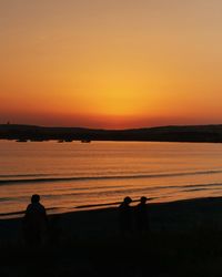 Silhouette people on beach against sky during sunset