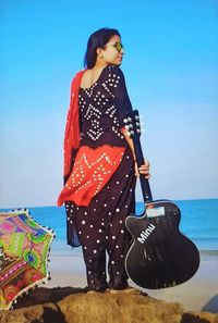 Young woman standing at beach against sky