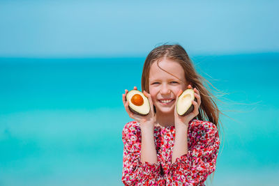 Portrait of a girl holding ice cream against blue sky