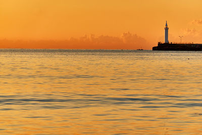 Lighthouse by sea against moody sky during sunrise