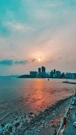 Sea and buildings against sky during sunset