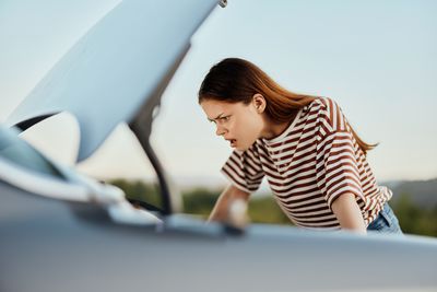 Side view of young woman sitting on car