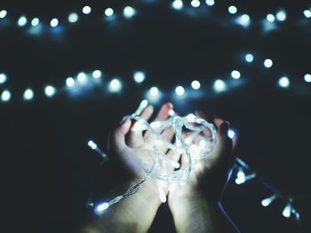 Close-up of hand holding illuminated string lights in darkroom
