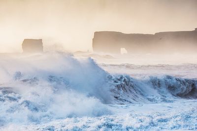 Sea waves splashing on shore against sky