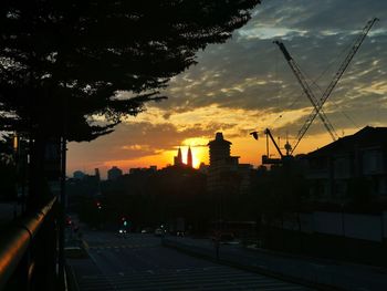 Silhouette city street by buildings against sky during sunset