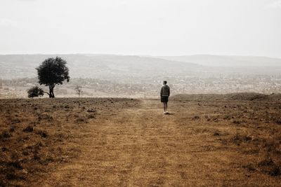 Rear view of man walking on field against sky