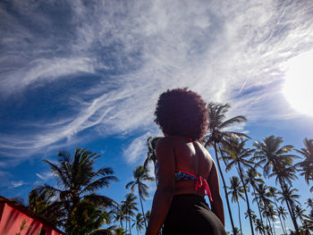 Rear view of woman standing by palm trees against sky. 
