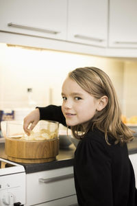 Side view portrait of girl eating potato chips at kitchen counter