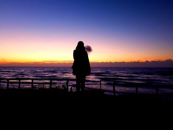 Silhouette couple standing at beach against sky during sunset