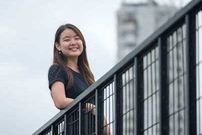 Young woman smiling while standing against railing