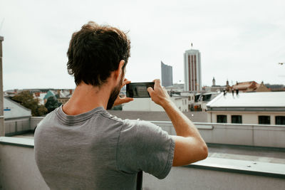 Rear view of man photographing city through mobile phone