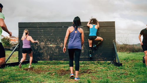 Rear view of women climbing wooden wall on land