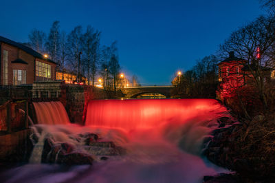 Illuminated building by river against sky at night