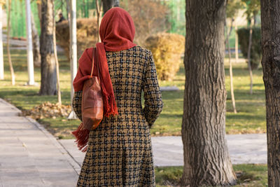 Rear view of woman standing by tree trunk