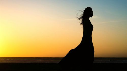 Silhouette woman standing on beach during sunset