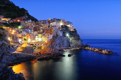 Illuminated houses on mountain by sea against sky during sunset