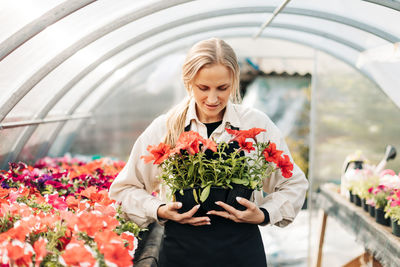 A young woman holds pots of flowers in a greenhouse. small business, garden center, flower shop