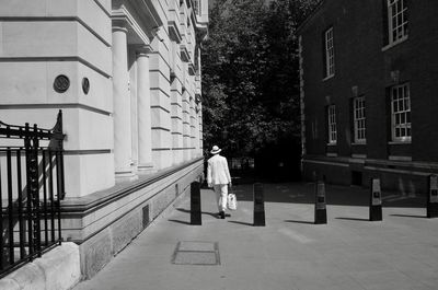 Rear view of man walking on footpath by building