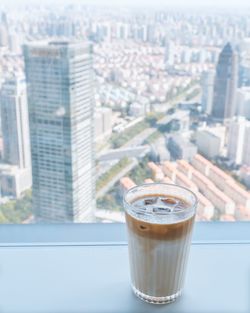 Glass of coffee on table against buildings in city