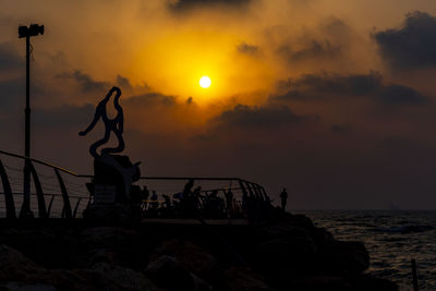 Silhouette rocks on beach against sky during sunset