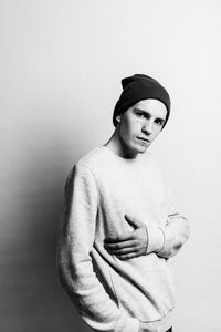 Portrait of young man wearing knit hat standing against white background