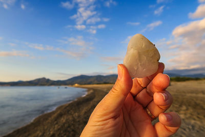 Midsection of person holding ice cream on beach against sky