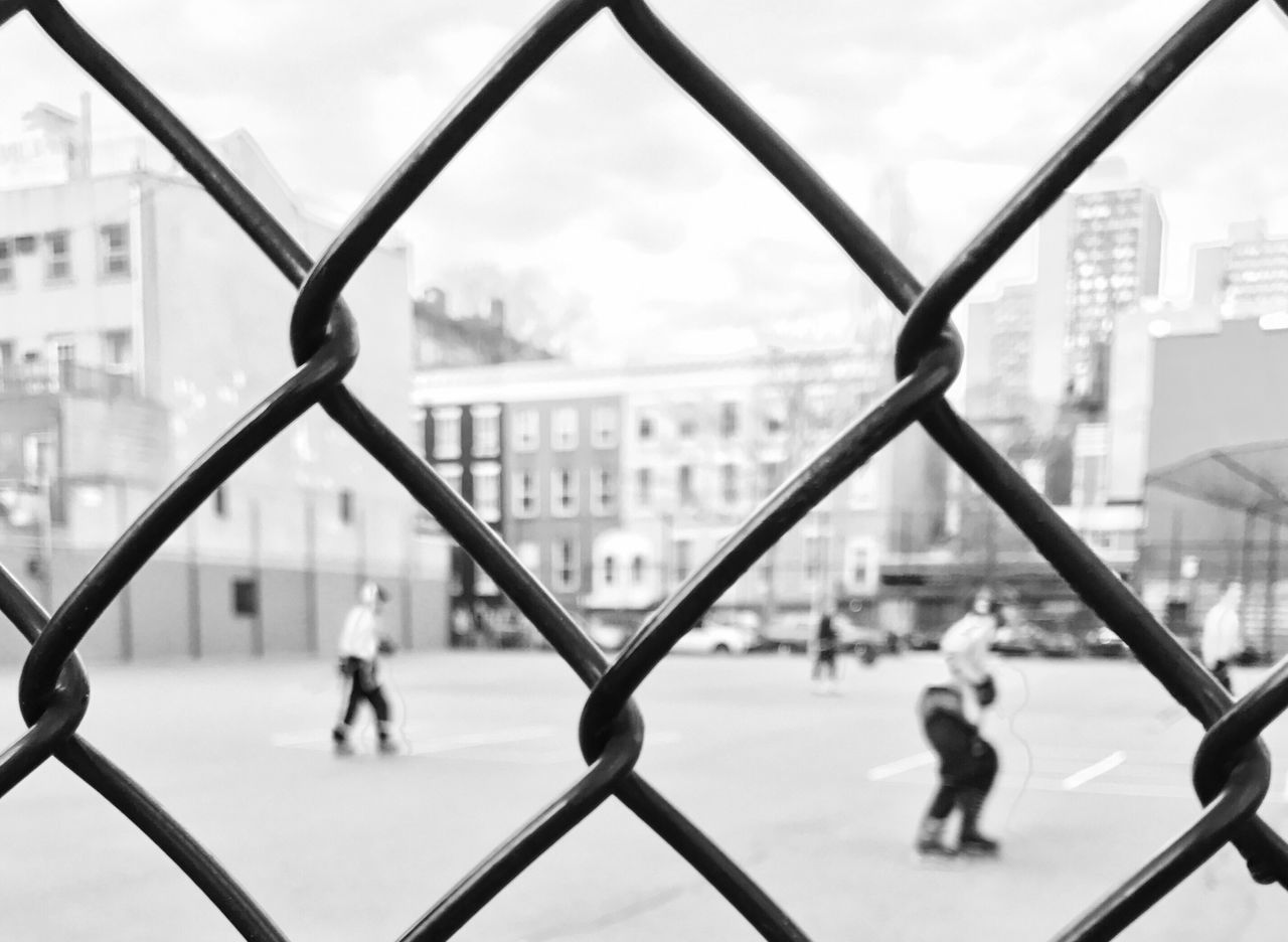chainlink fence, day, playing, city, building exterior, real people, outdoors, architecture, focus on foreground, group of people, basketball - sport, built structure, court, team sport, sport, sky, childhood, close-up, competitive sport, soccer field, people