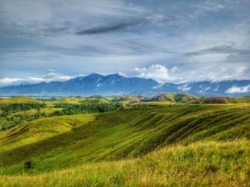 Scenic view of green mountains against cloudy sky