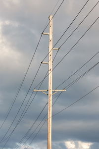 Low angle view of electricity pylon against cloudy sky