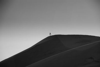 Low angle view of silhouette person standing on sand dune against clear sky