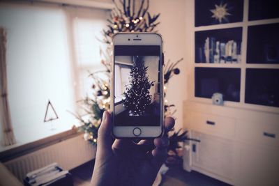 Close-up of hand photographing christmas tree through smart phone at home