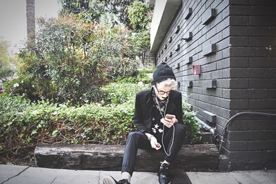 Man using mobile phone while sitting on wood by house