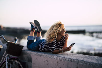 Midsection of man using mobile phone by sea against sky