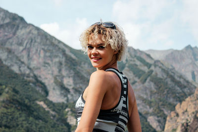 Portrait of smiling young woman standing against mountain range