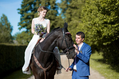 Young bridegroom standing by bride sitting on horse