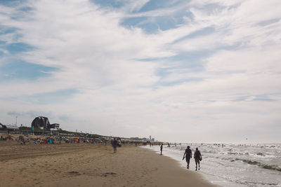 People walking at sea shore against sky