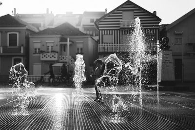 Full length of boy splashing water against houses in city