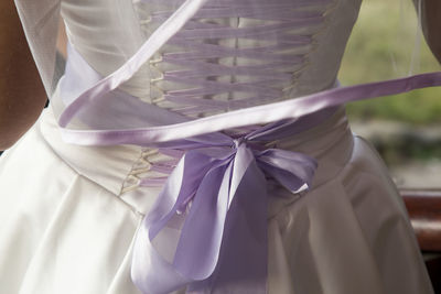 Midsection of woman in wedding dress standing by window