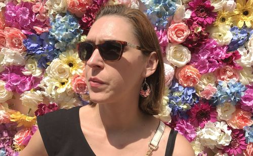 Woman in sunglasses standing against colorful flower decoration