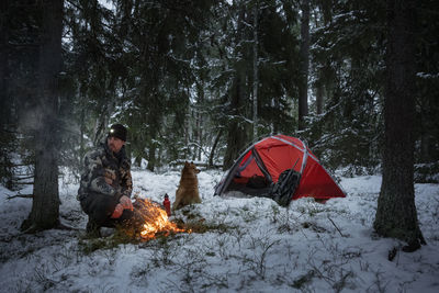 Man in winter forest in front of log fire